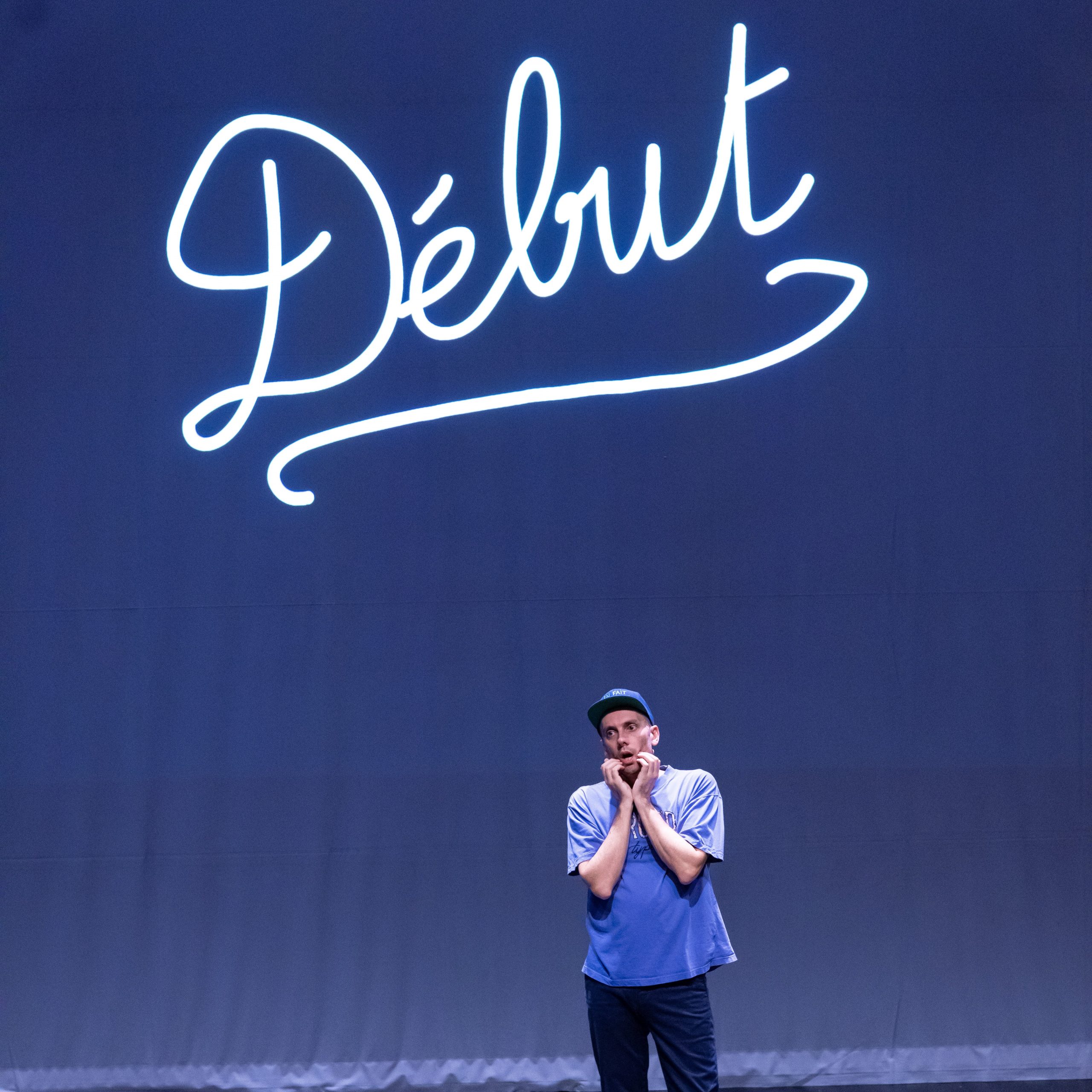 Antoine defoort sur scène. Derrière lui, un écran avec écrit le mot "Début"